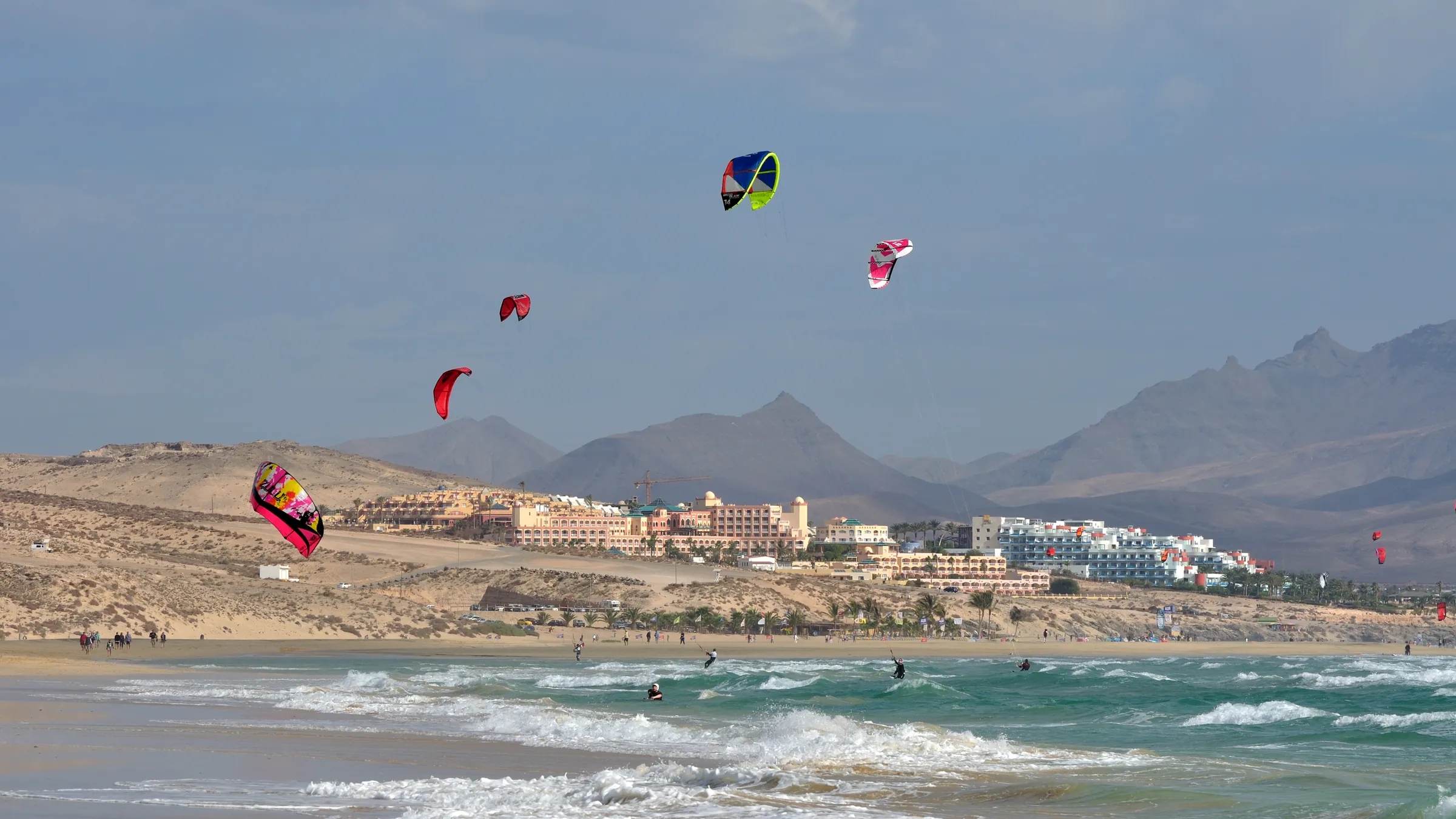 Kleurige kites boven het strand van Sotavento, met hotels en de bergen van Jandía erachter