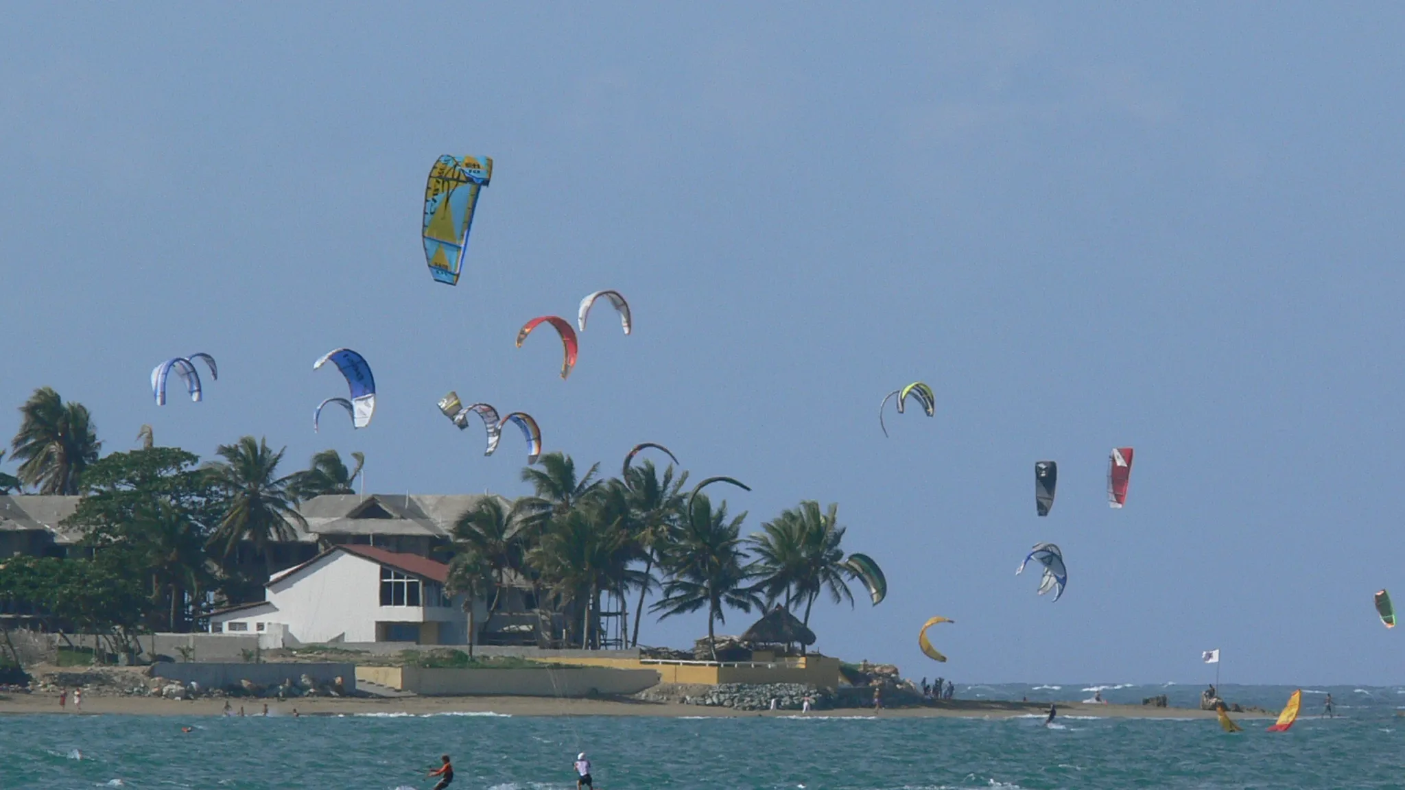 Tientallen kites boven de baai van Cabarete, met palmen en huizen aan de waterkant