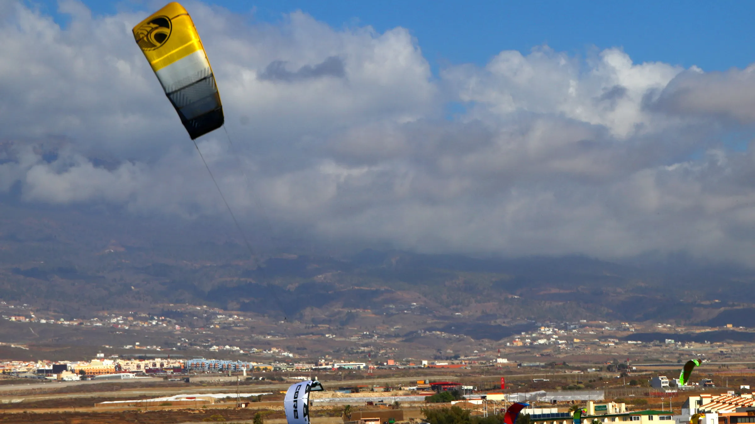 Kite boven het strand van El Médano, met het dorp en de bergen van Tenerife onder de wolken