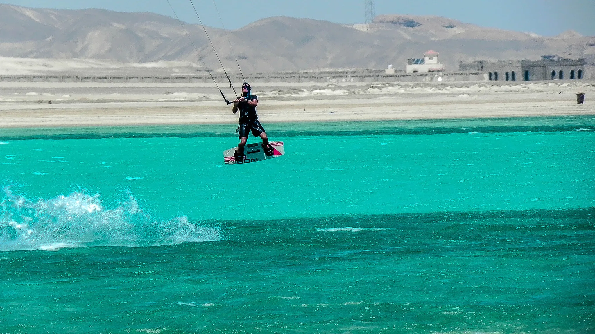 Kitesurfer springt boven turquoise water bij Marsa Alam, met woestijnbergen erachter