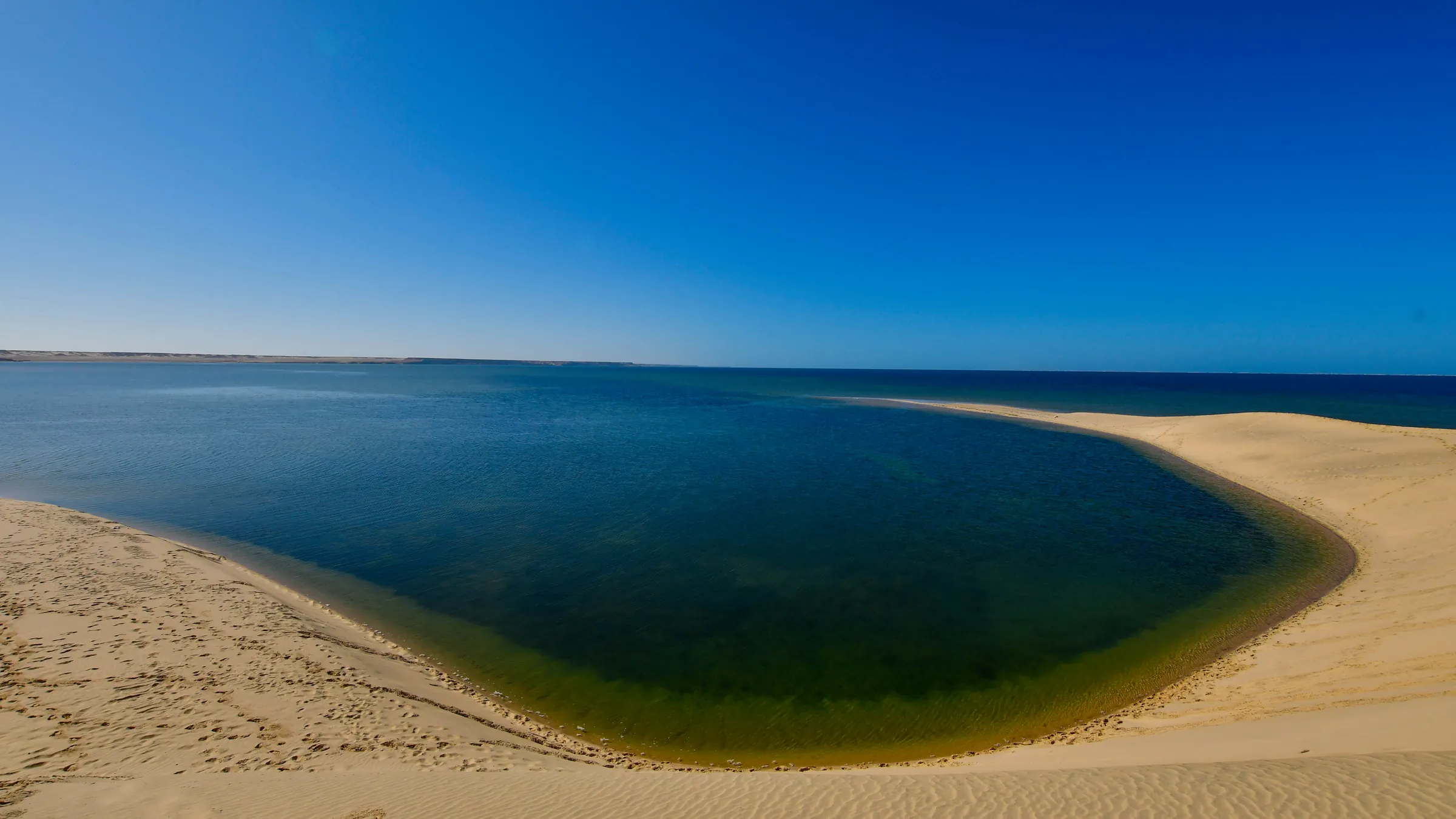 Diepblauwe baai tussen witte zandduinen aan de lagune van Dakhla