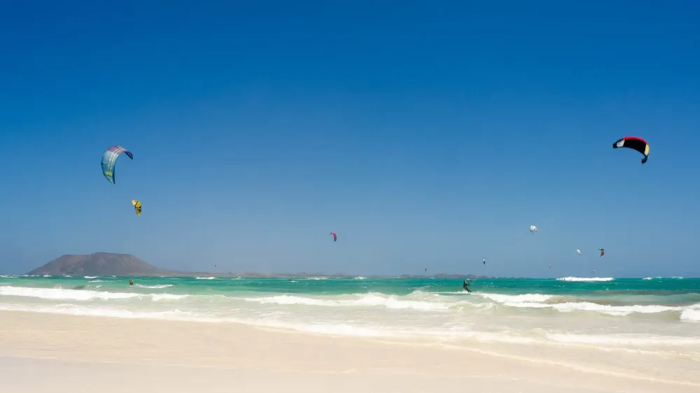 Kites boven het turquoise water van Flag Beach bij Corralejo, met het eilandje Lobos aan de horizon