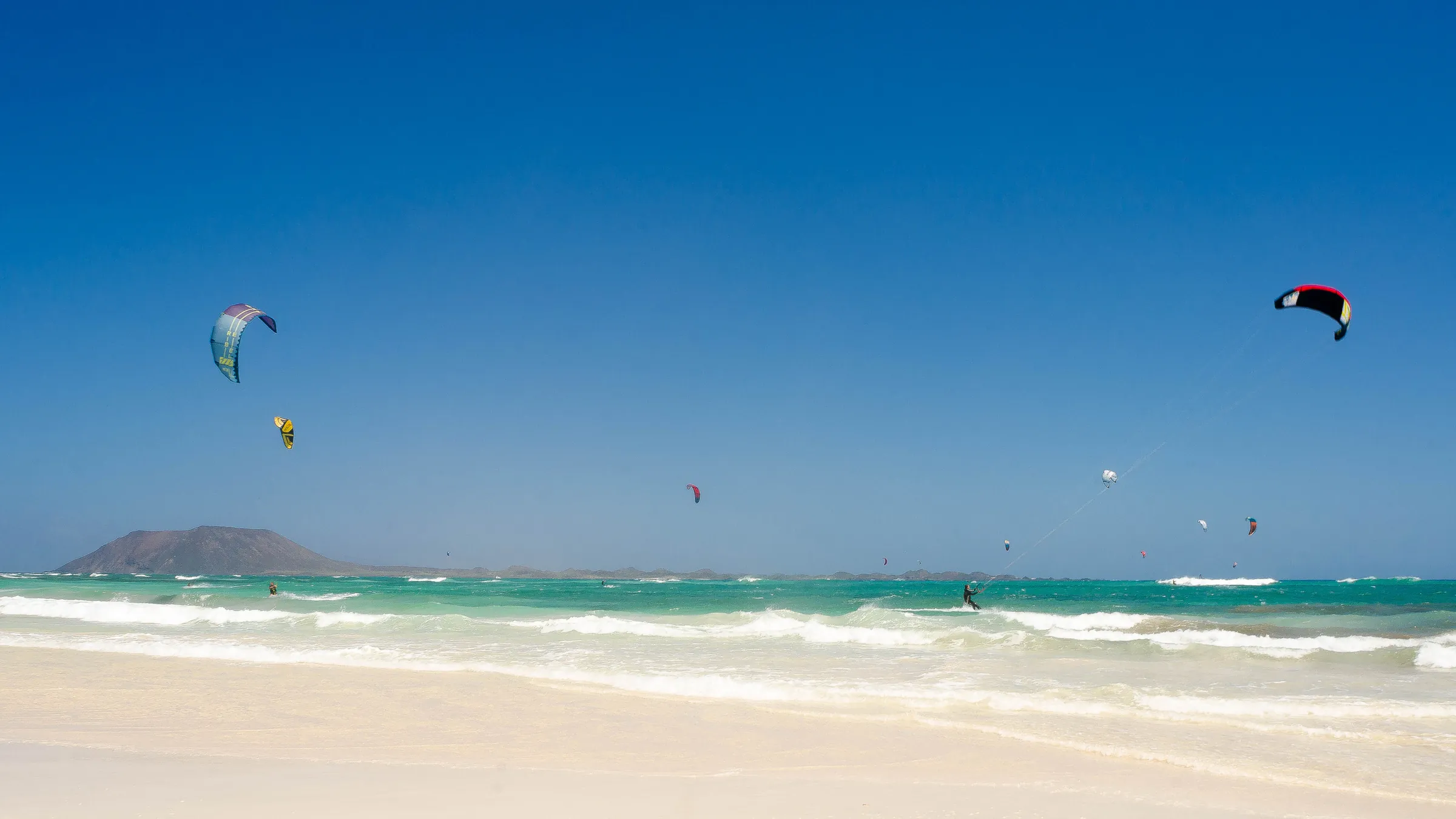 Kites boven het turquoise water van Flag Beach bij Corralejo, met het eilandje Lobos aan de horizon
