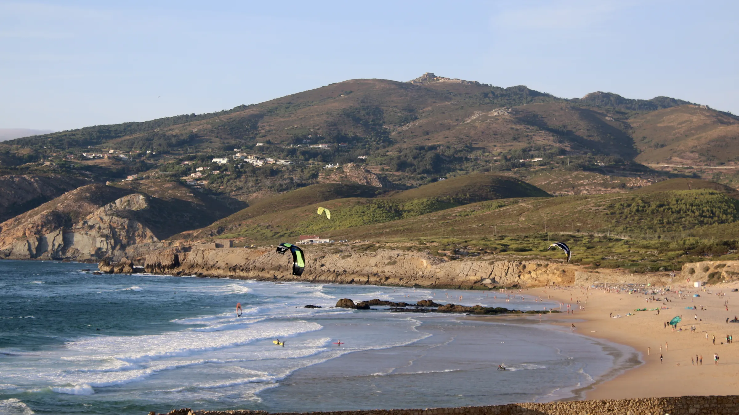 Het strand van Guincho van bovenaf, met kites boven de baai en de Serra de Sintra erachter