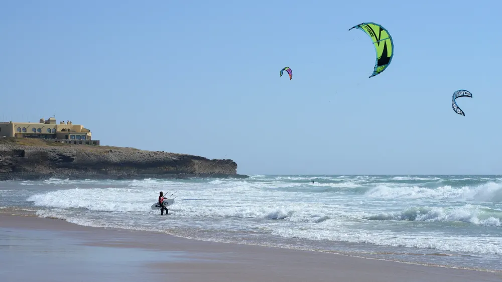 Kites boven de golven van Praia do Guincho, met een kiter die met zijn board de zee uit loopt