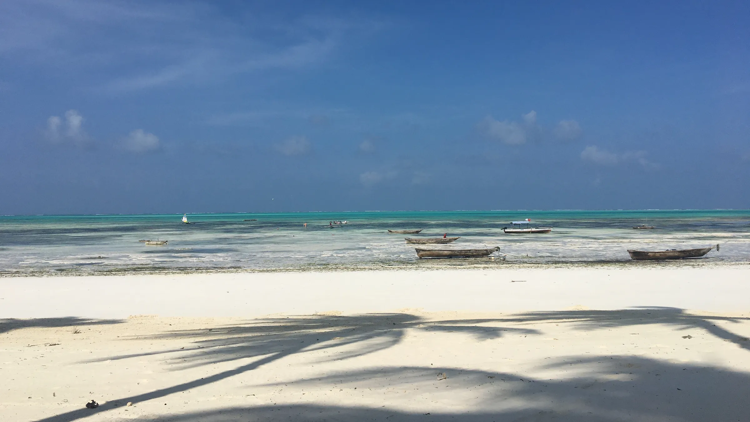 Wit strand en turquoise lagune bij Jambiani met vissersboten bij laag water