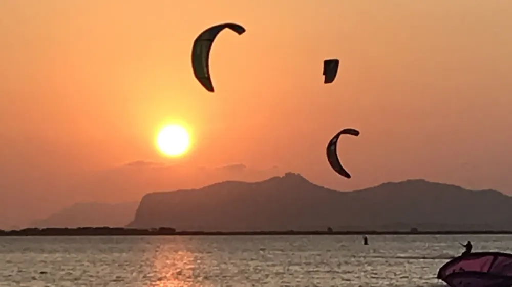 Kites bij zonsondergang boven de lagune van Lo Stagnone, met de bergen bij Trapani op de achtergrond