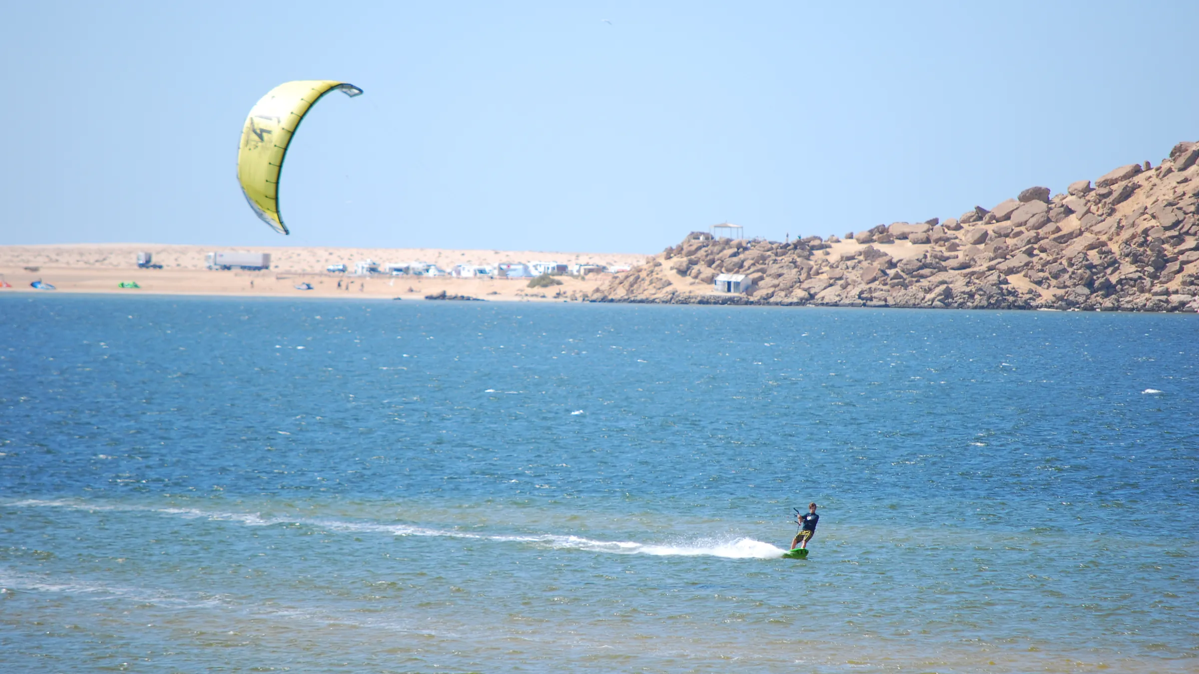 Kitesurfer met een gele kite op de lagune van Dakhla, met de kust en een rotsheuvel op de achtergrond