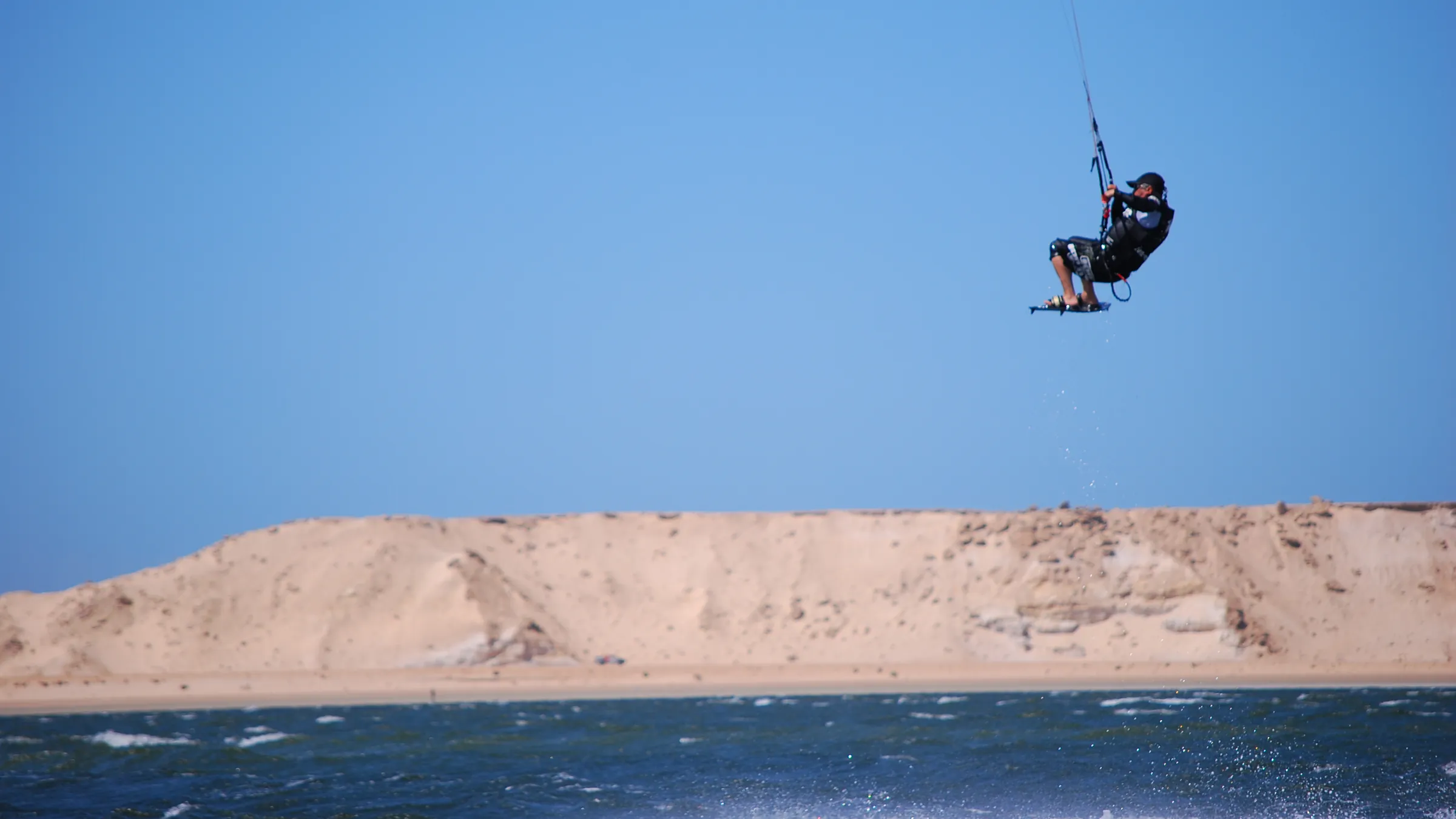 Kitesurfer hoog in de lucht boven een zandduin bij Dakhla