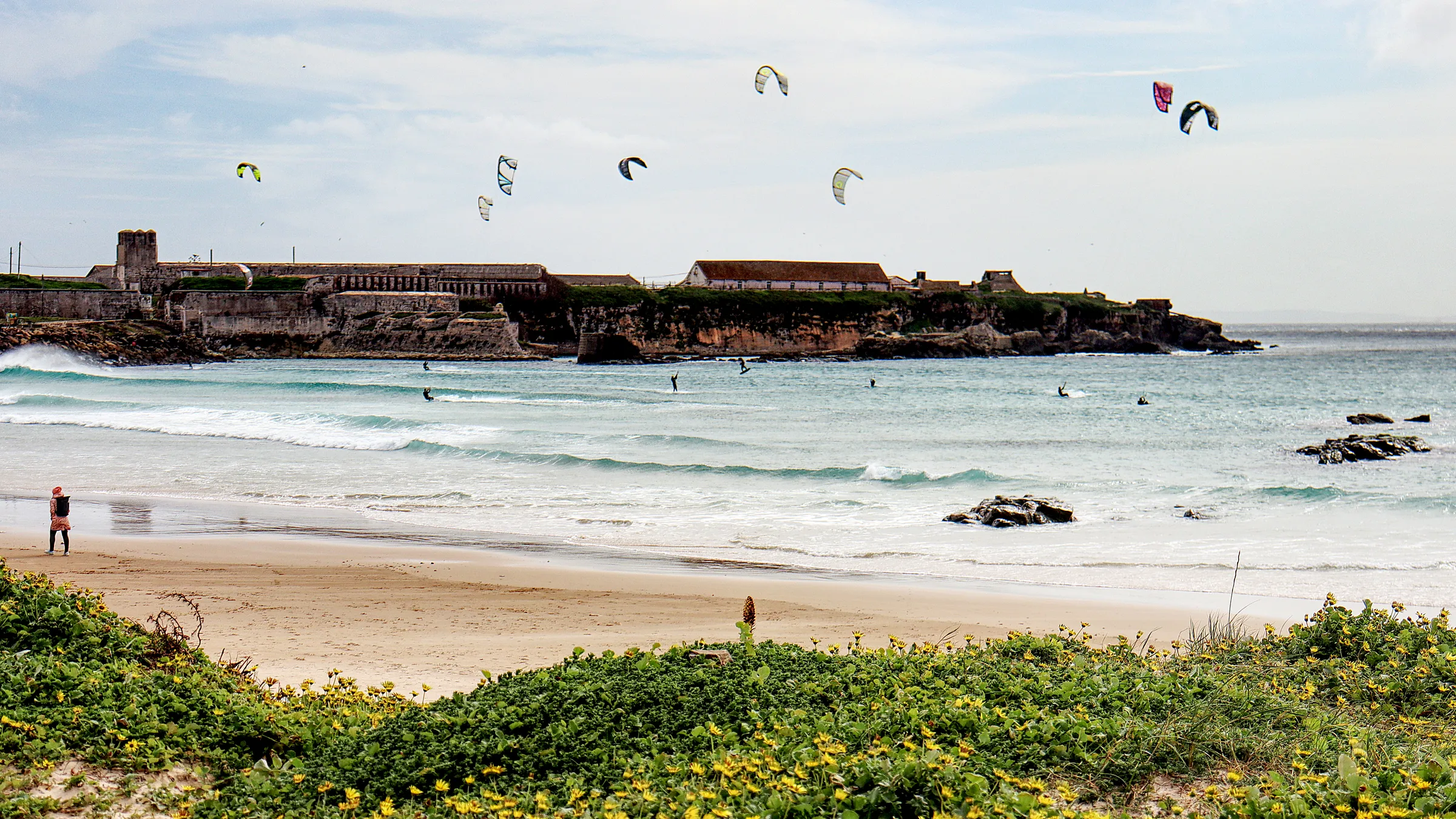 Kitesurfers op zee voor het eiland Las Palomas bij Tarifa, met de branding en het strand op de voorgrond