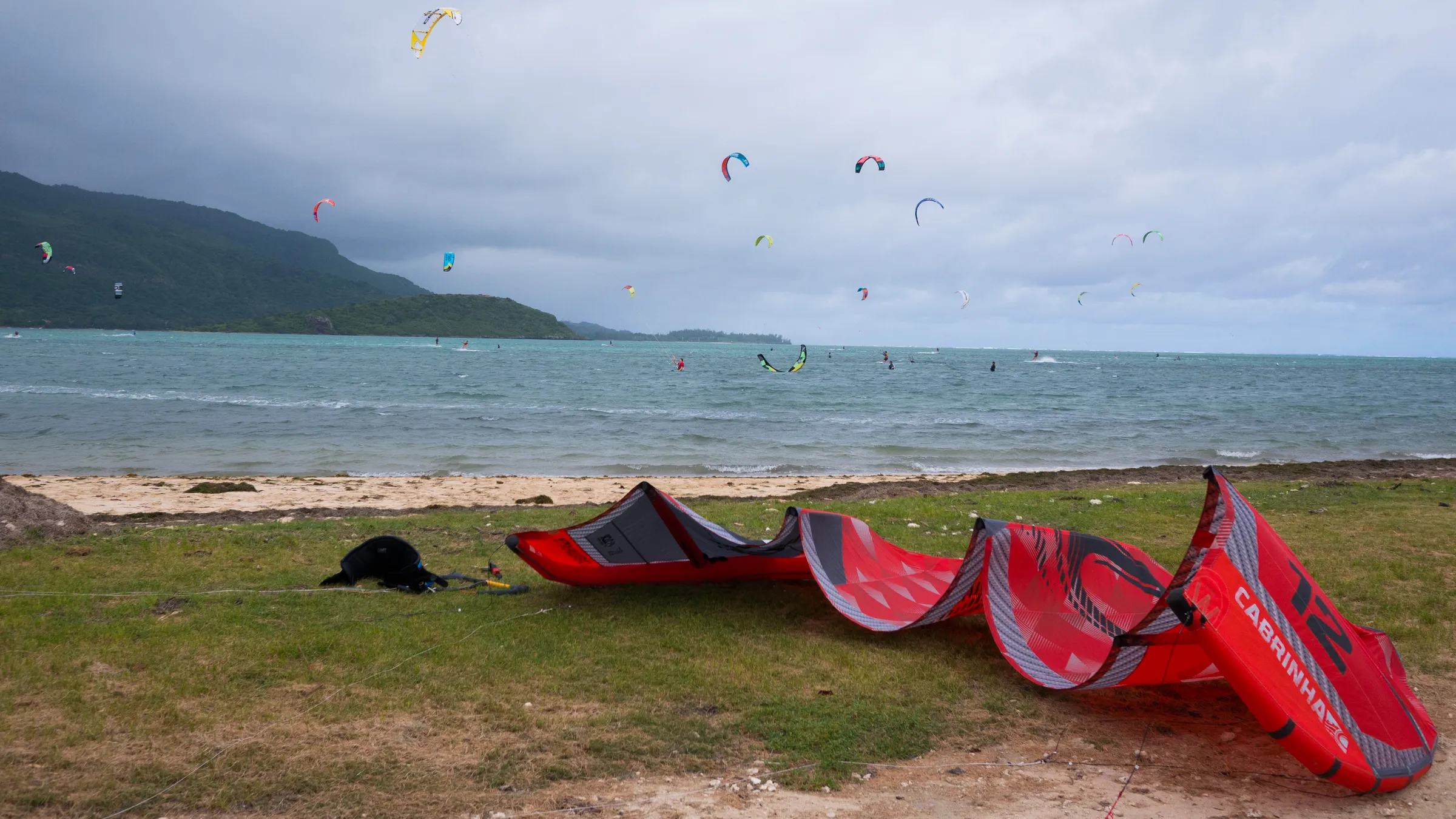 Tientallen kites boven de lagune van Le Morne, met een kite op het gras aan de waterkant