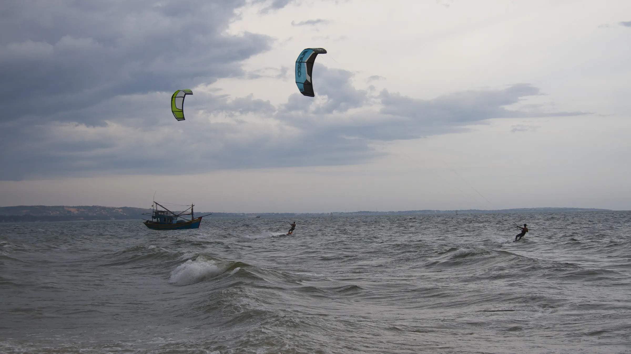 Kitesurfers en een vissersboot op de golvende zee bij Mui Ne