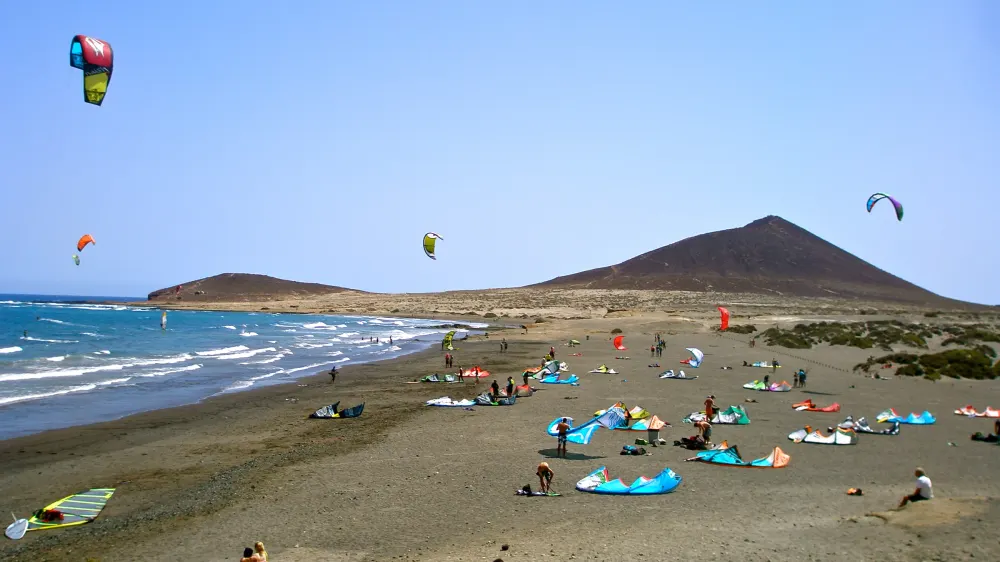 Kites in de lucht en op het strand van El Médano, met Montaña Roja op de achtergrond