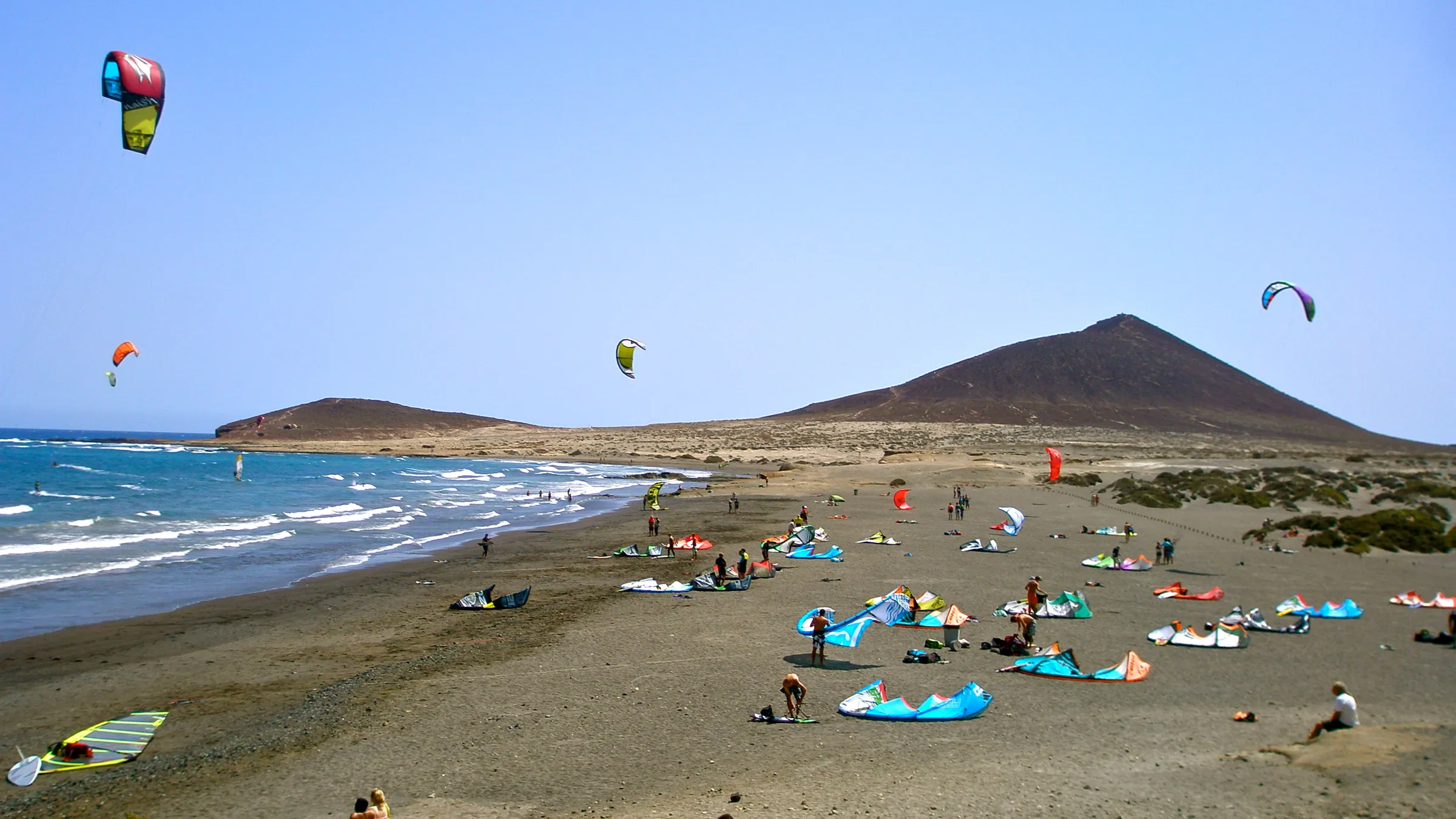 Kites in de lucht en op het strand van El Médano, met Montaña Roja op de achtergrond