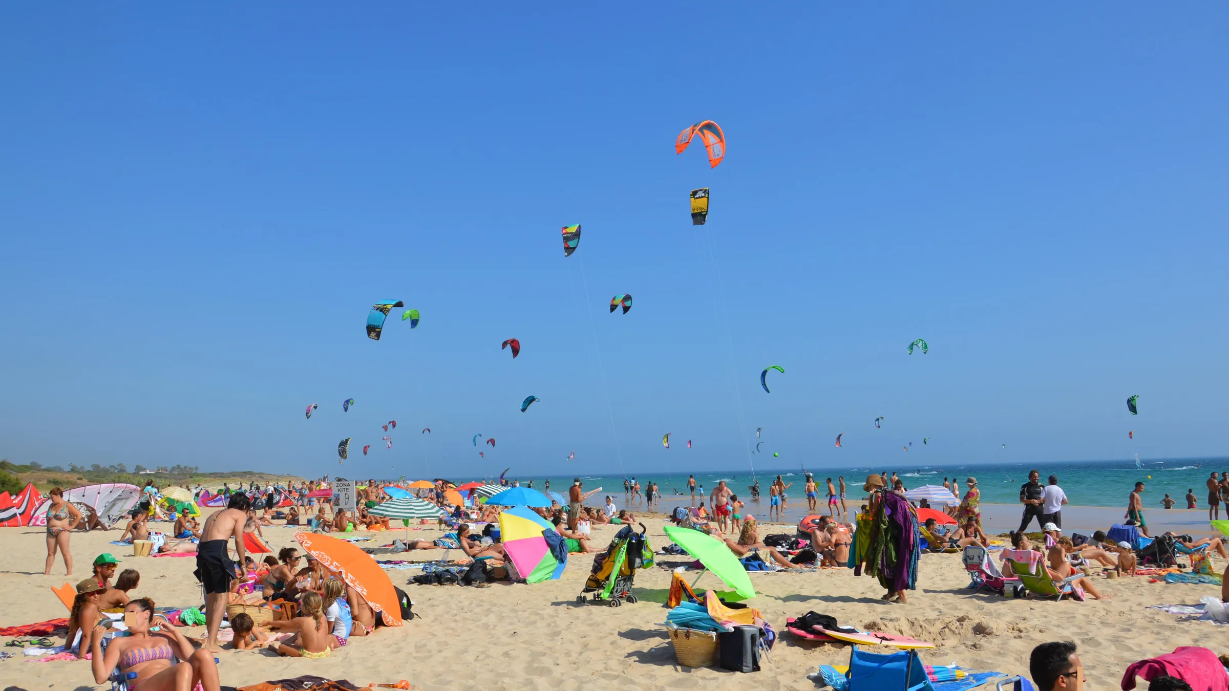 Een druk zomerstrand in Valdevaqueros met veel kites in de lucht