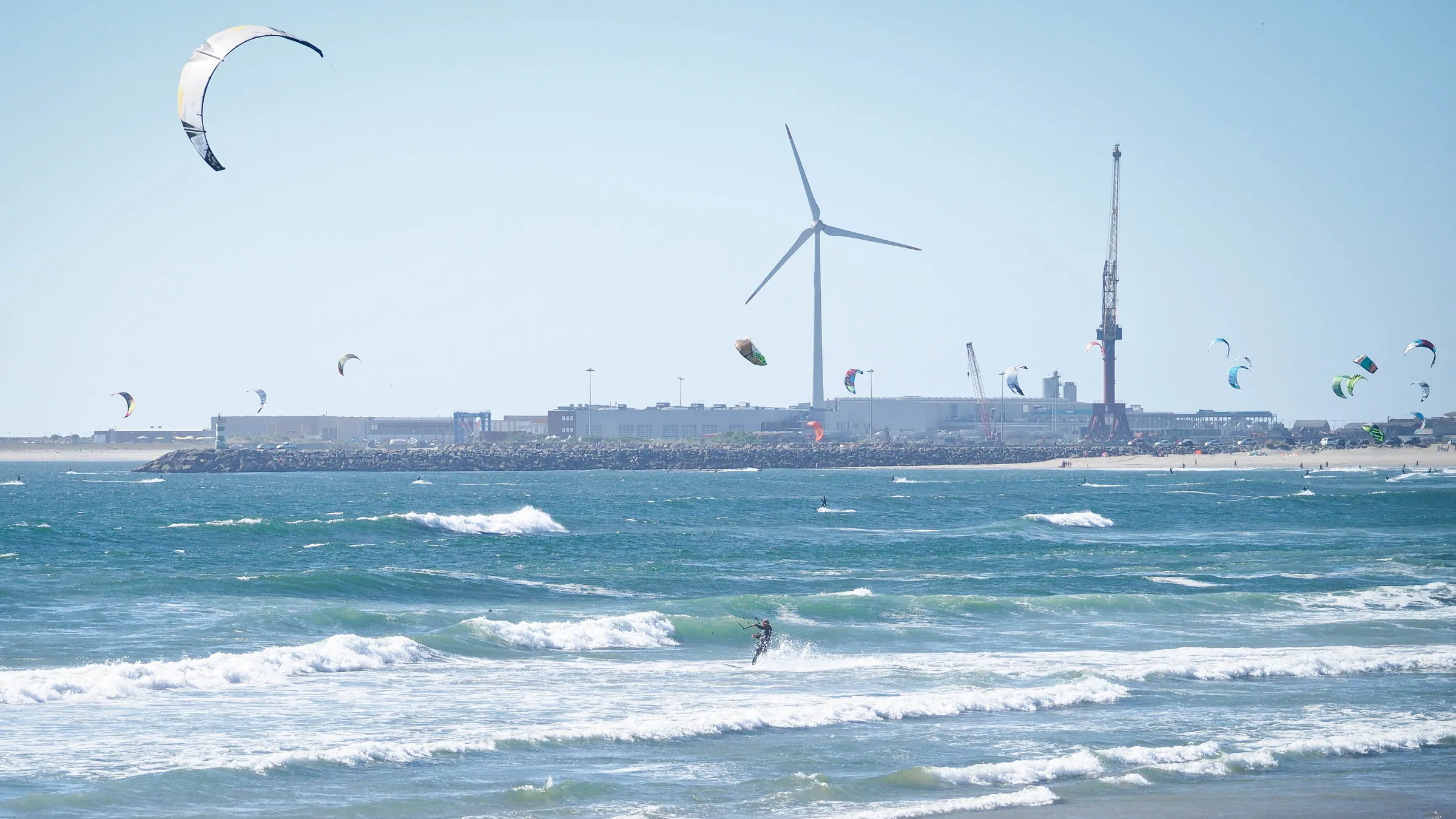 Tientallen kites voor de havenpier van Viana do Castelo, met een windturbine en havenkranen