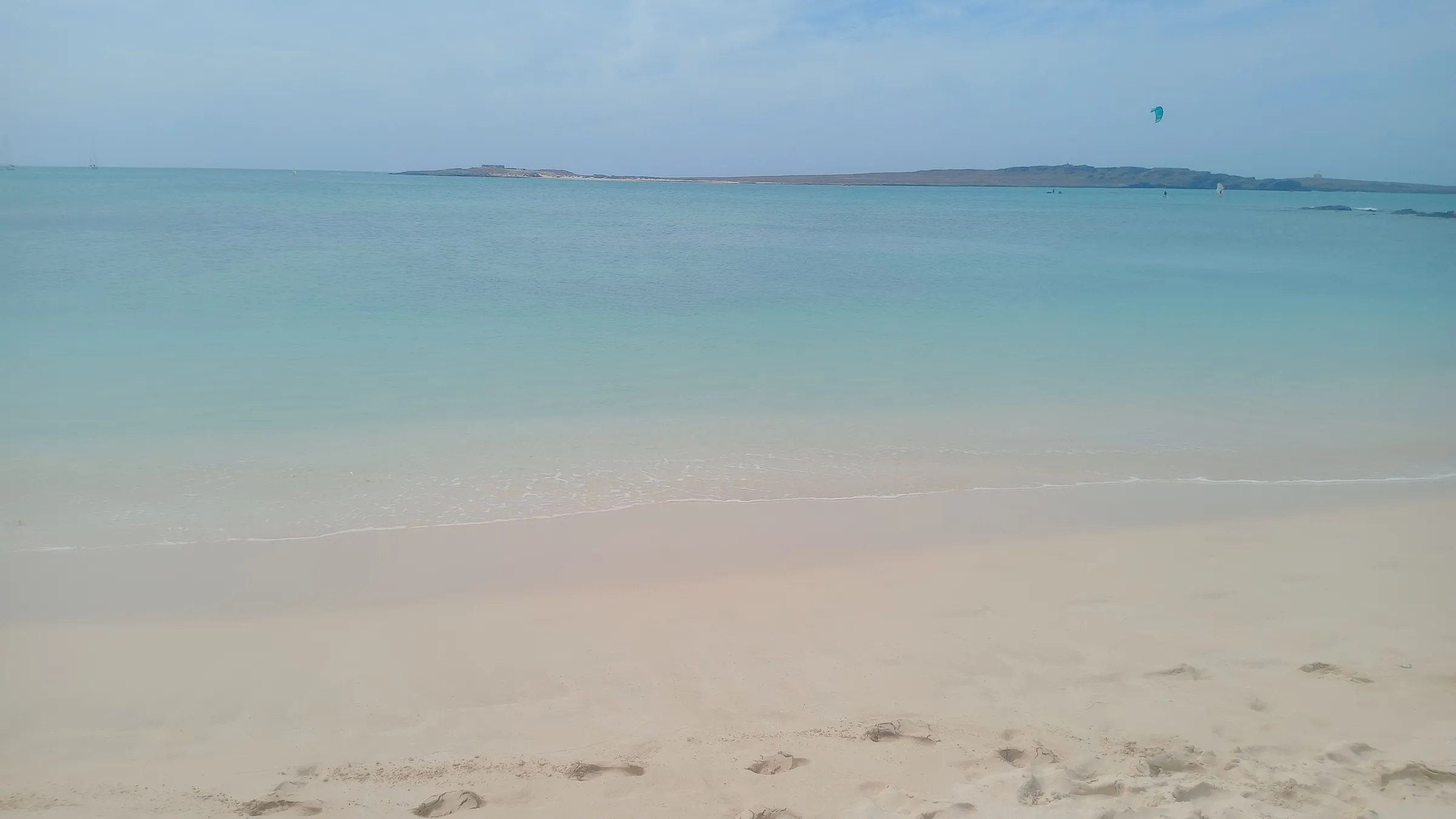 Vlak turquoise water bij Praia de Estoril bij Sal Rei, met een kite in de verte