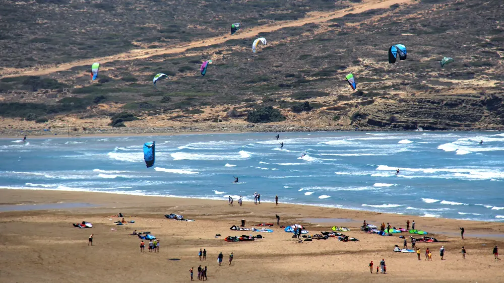 Kites boven de golfkant van Prasonisi, met kites en kiters op het zandstrand