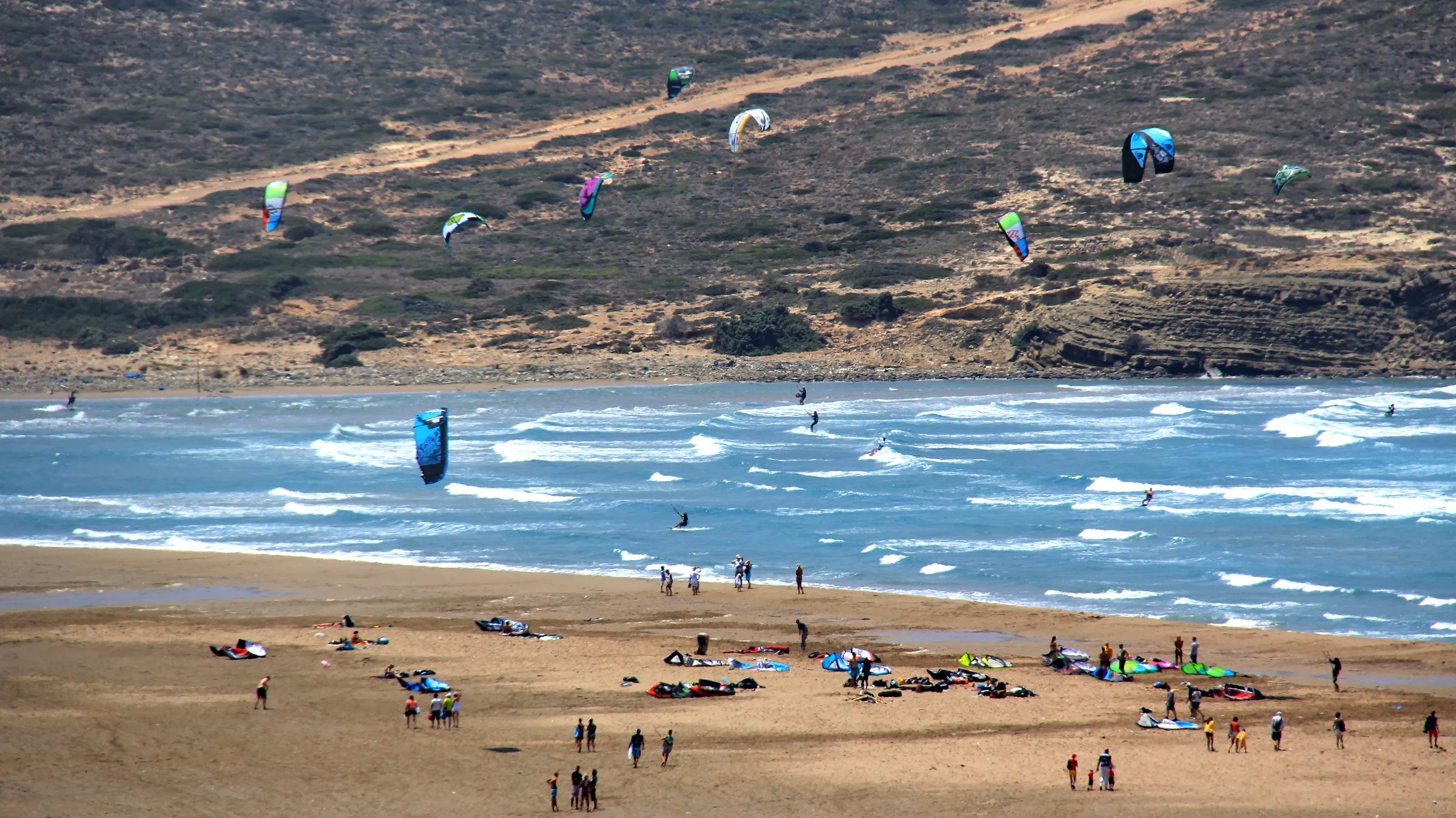 Kites boven de golfkant van Prasonisi, met kites en kiters op het zandstrand