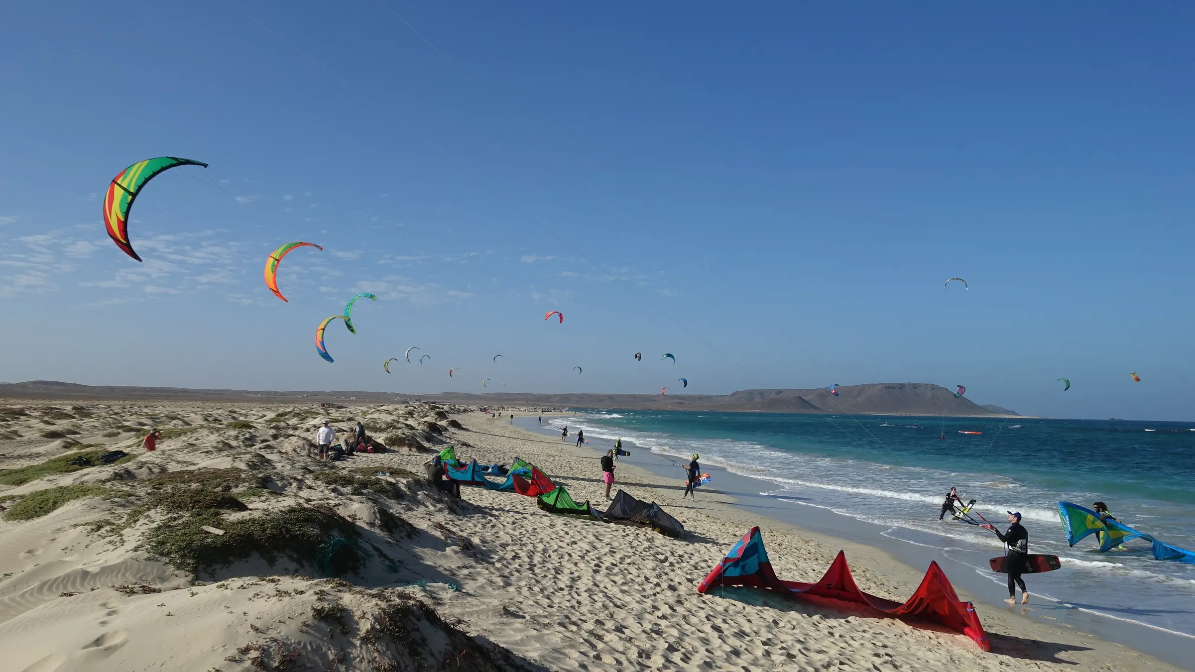 Kites in de lucht boven het strand aan de oostkust van Sal, met kites op het zand en de bergen in de verte