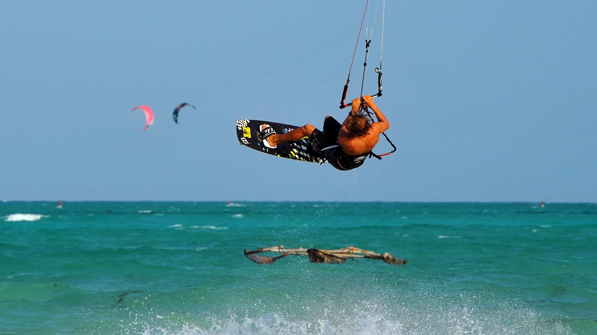Kitesurfer in de lucht boven turquoise water bij Zanzibar, met kites en een dhow op de achtergrond